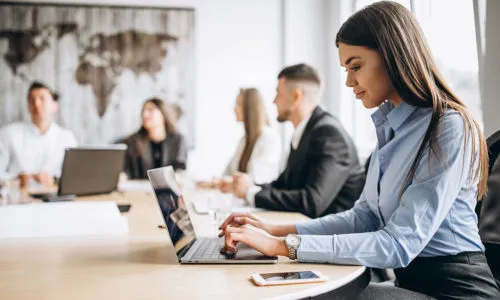 Equipe em reunião, com uma profissional usando o notebook em primeiro plano